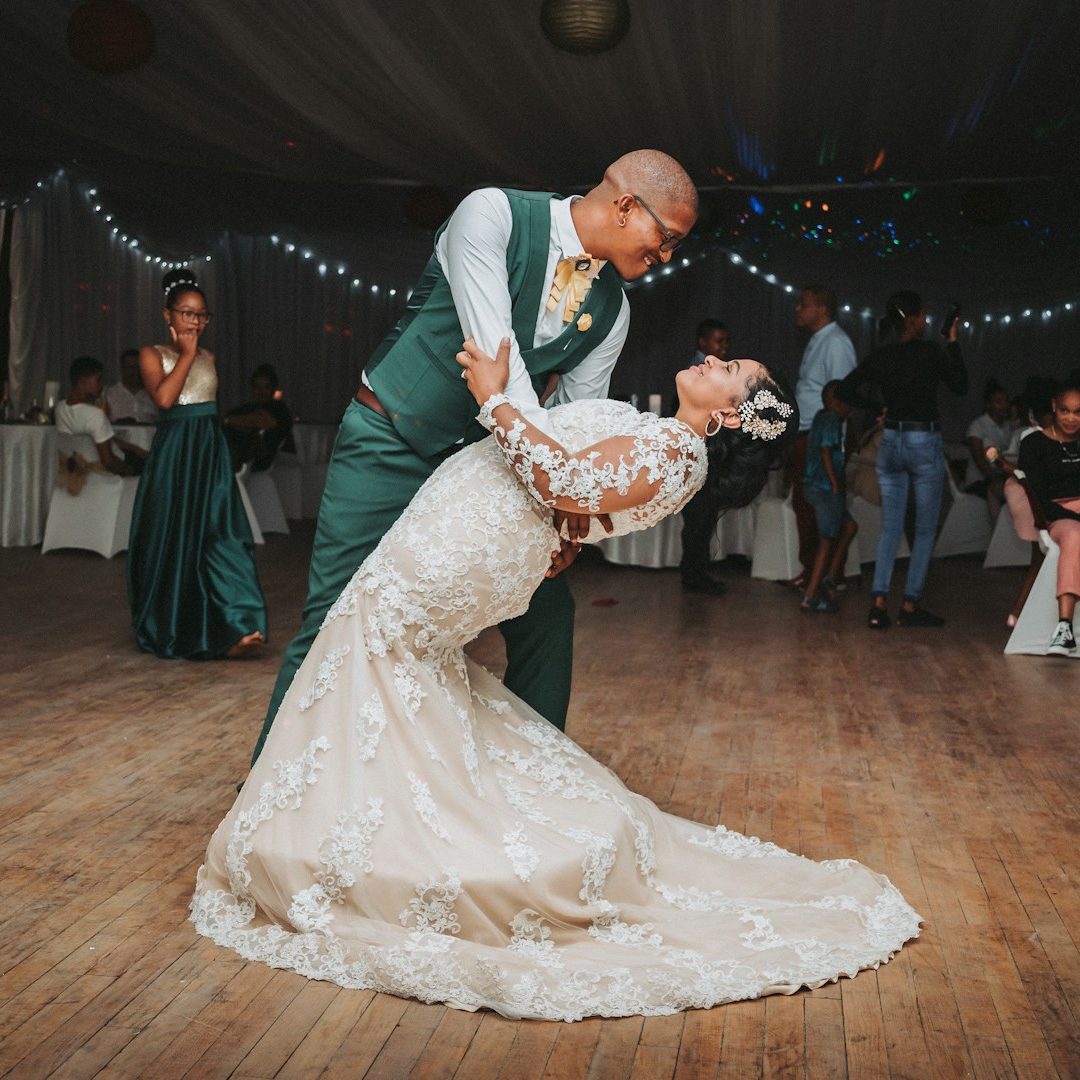 A couple shares a romantic dance, the bride in a lace gown and the groom in a green suit.