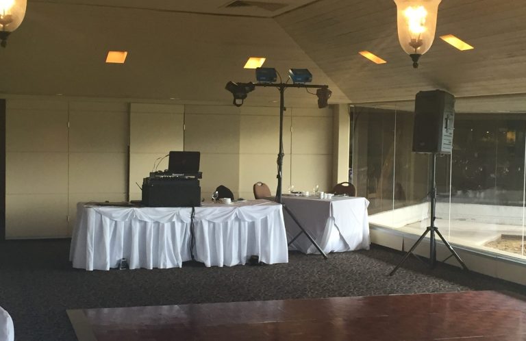 Wedding DJ Package Event space with a DJ setup, speakers, and tables in a well-lit room.