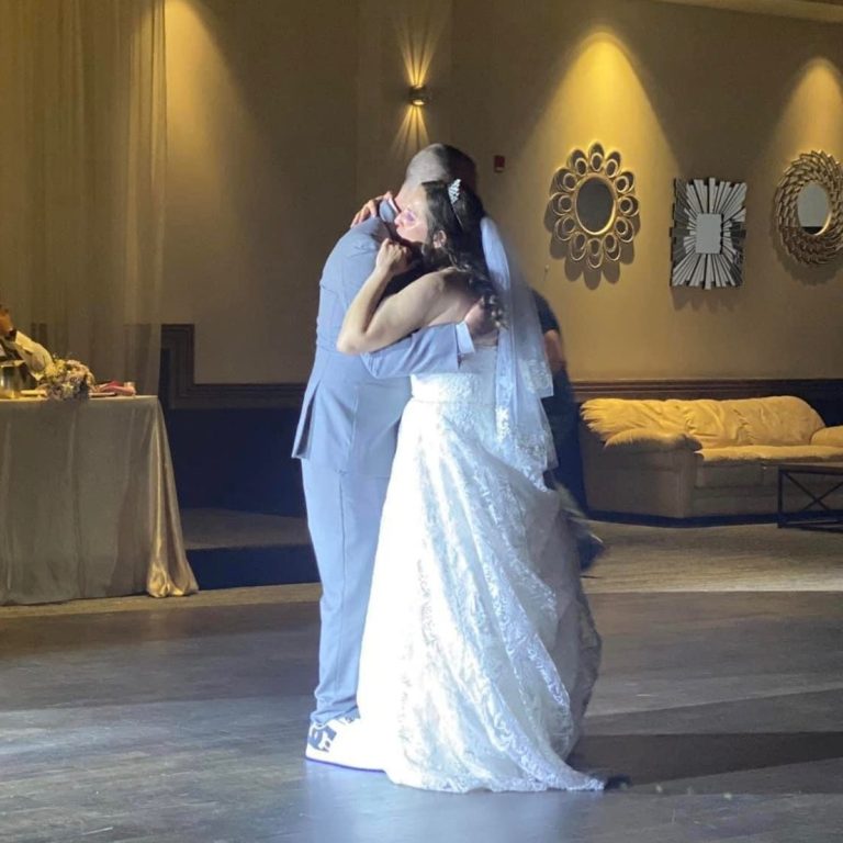 Bride and groom share a dance, dressed elegantly in a softly lit reception venue.
