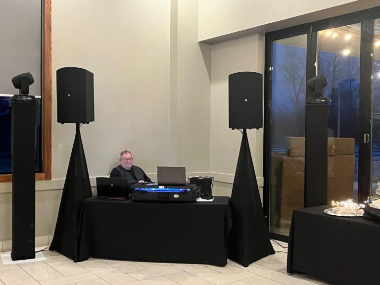 A DJ at a setup with speakers and a laptop in a modern event space.