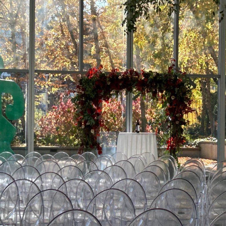 Empty chairs arranged for a wedding ceremony under a floral arch in a garden setting.