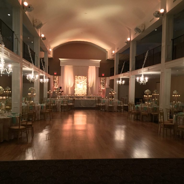 Elegant banquet hall with warm lighting, wooden floor, and tables set for an event.