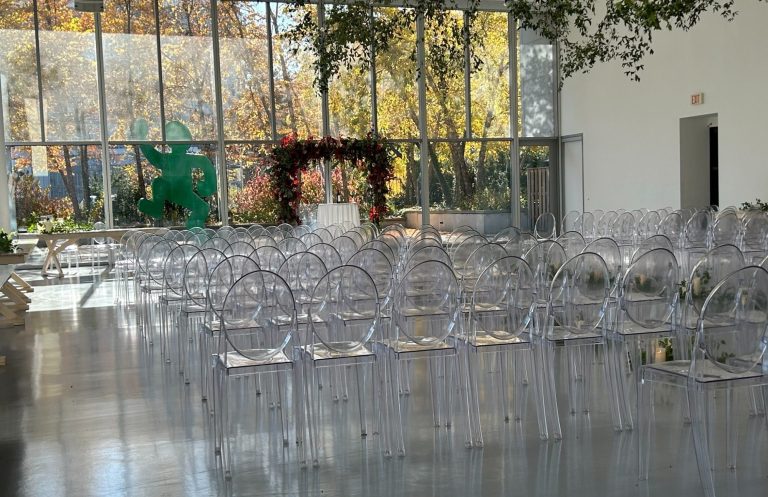 Wedding Ceremony A spacious venue set up with clear chairs for an event, featuring a floral backdrop.